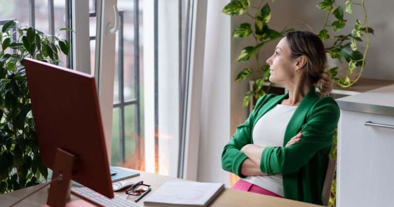Young woman sitting at a computer desk, pausing to look out the window, reflecting on how gut health and mental clarity are connected.