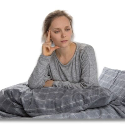 A woman is sitting in bed with her hand on her face and looking ill because she is experiencing candida die-off symptoms
