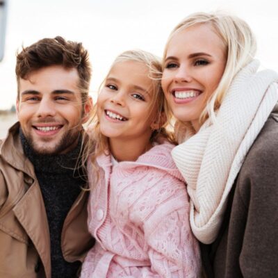 A man, a woman, and a girl smile at the camera outdoors, all wearing warm clothing.