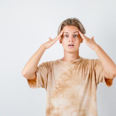 Teenage boy in a baggy T-shirt holding his head with both hands, looking confused and blank, symbolizing brain fog linked to poor gut health and Candida.