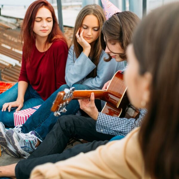 Small group of young people sitting together with guitar representing social connections for stress management and health improvement