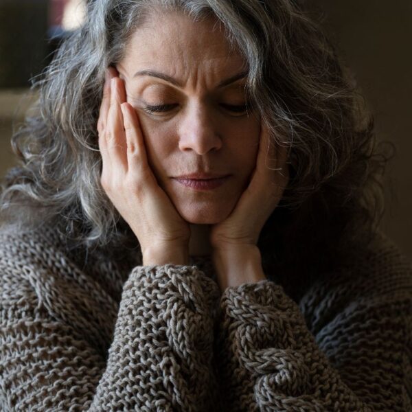 A woman sitting with her head in her hands, looking down, conveying fatigue, stress, or mental overwhelm.