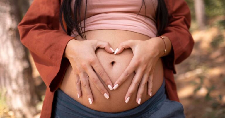 Pregnant woman forming heart shape on belly with hands