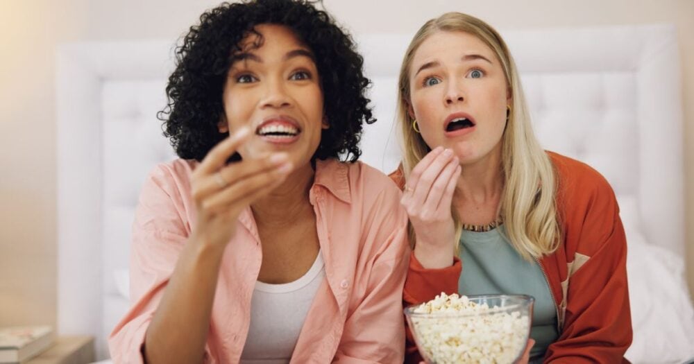 Two young women sitting together enjoying a bowl of popcorn, illustrating the question “Can I eat popcorn on the Candida diet?