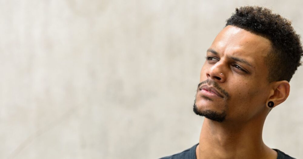 Young male standing against a wall, head tilted back slightly with a questioning expression, representing the question: is a male yeast infection contagious?