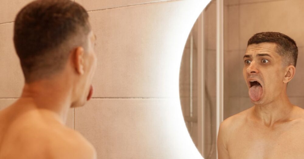 Man checking his tongue in the mirror for signs of oral thrush; symptoms of male oral yeast infection.
