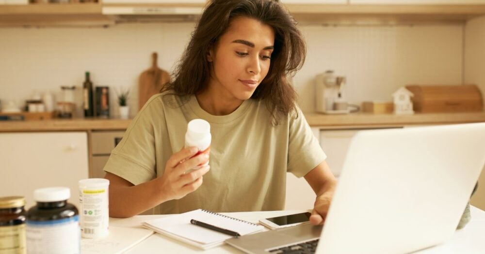 Young woman researching the best probiotic for candidiasis while holding a daily probiotic supplement.