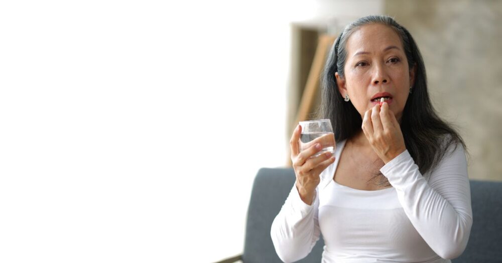 asian woman holding up a glass of water and taking some digestive enzymes to support candida cleansing.