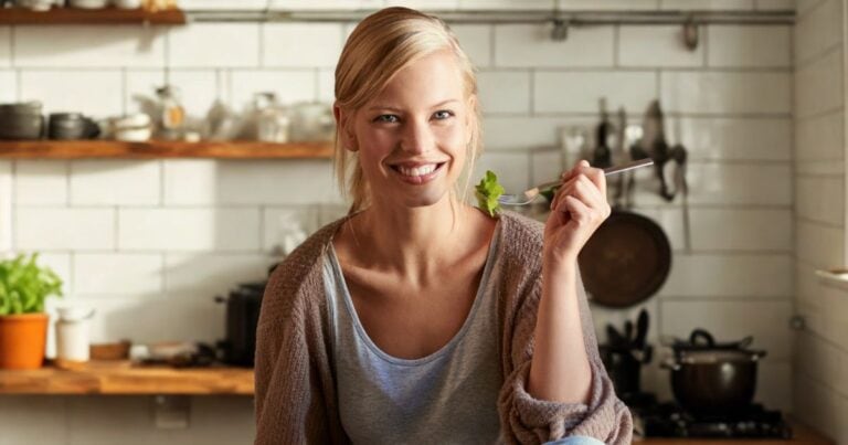 oman in a kitchen holding a fork with leafy green vegetables, practicing mindful eating to reduce sugar cravings.