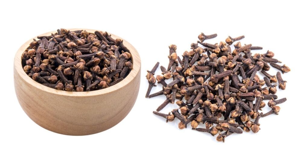 Close-up of cloves and a wooden bowl of cloves on a bench, illustrating clove for candida and clove for yeast infection.