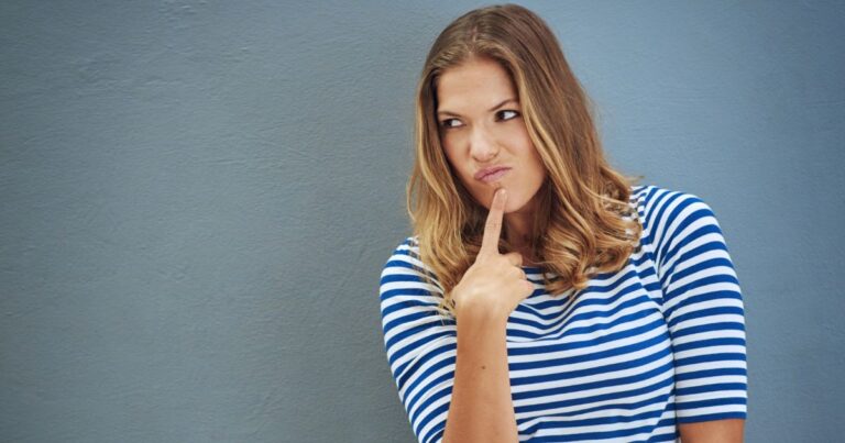 Close-up of a young woman looking thoughtfully to the side, finger on her chin, representing curiosity and contemplation about vaginal health and differences between vaginitis and yeast infection.