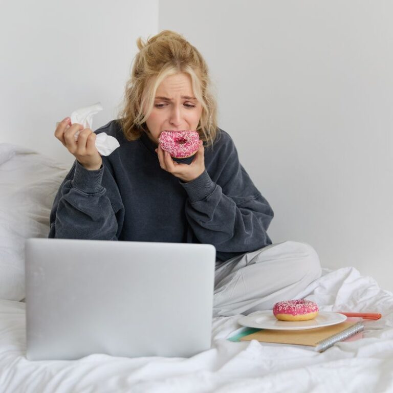 young girl sitting on bed infront of computer eating sweet stuffs and wondering if she is experiencing candida die-off or something else