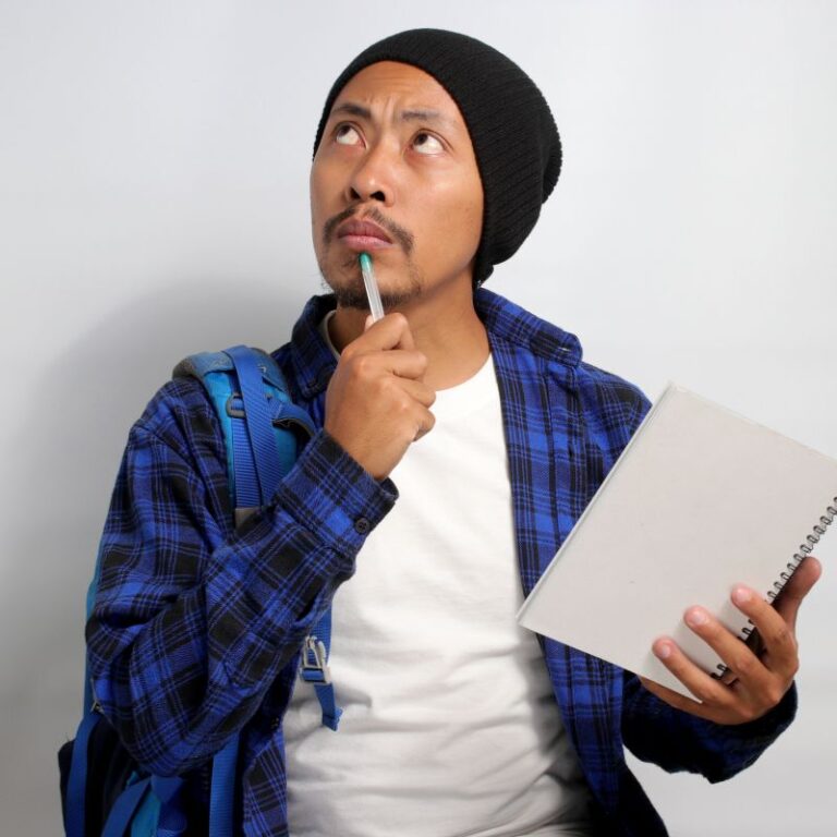 young man with a beanie on holding a notebook and looking skyward possibly wondering what are systemic enzymes