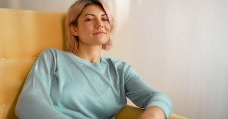 Young woman sitting relaxed in a chair, smiling at the camera, representing calm and mental wellbeing supported by gut health.