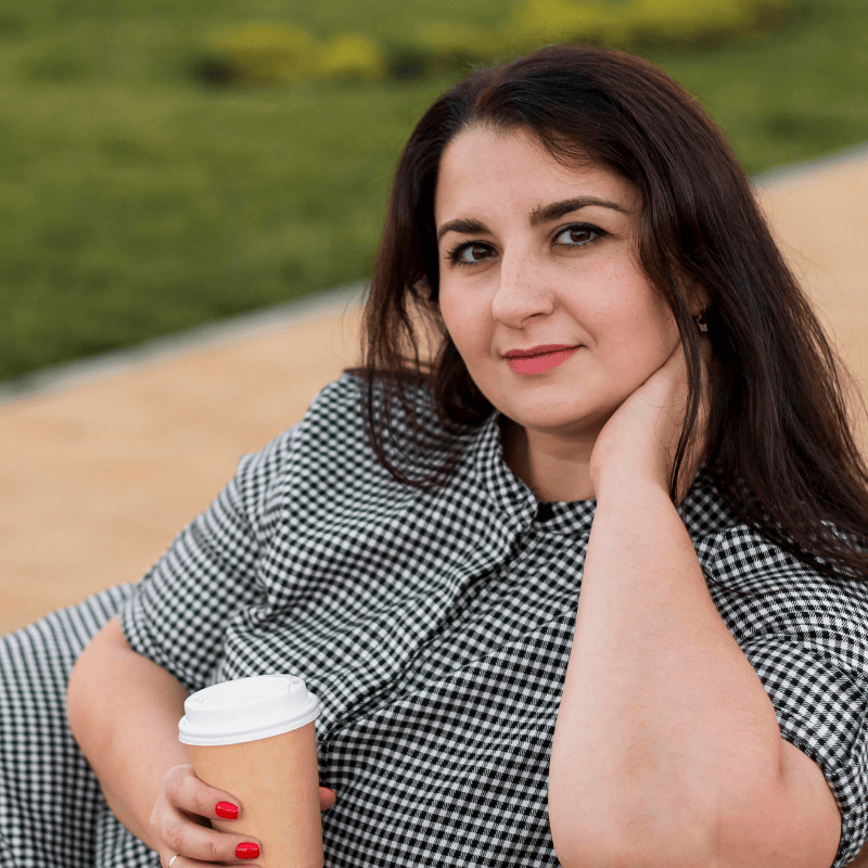 woman sitting outside drinking a coffee and likely wondering what causes her IBS Symptoms