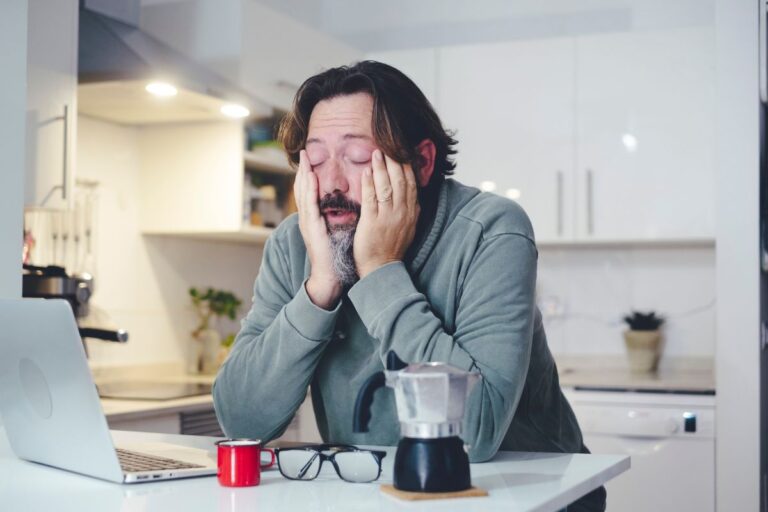 very tired male sits at kitchen bench with head in both hands - candida and fatigue