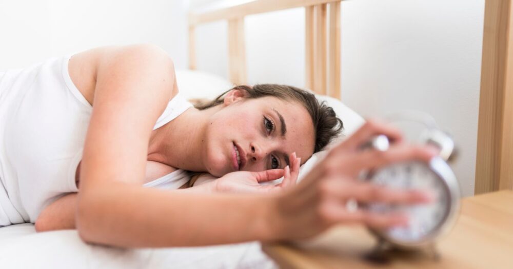 a woman turning her alarm clock off waking up tired - candida and sleep
