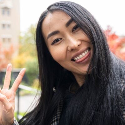 attractive female asian woman with big smile giving doing the peace symbol as an example of how you feel when the gut makes brain chemicals