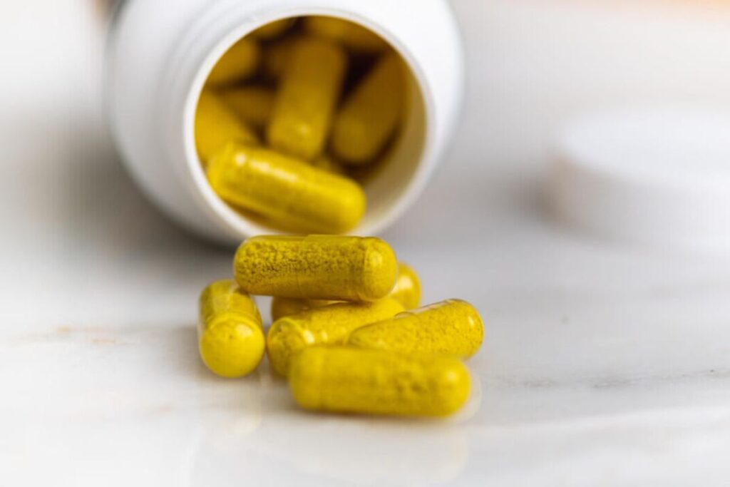 An open white bottle with yellow capsules spilling onto a white surface, with the bottle cap nearby.